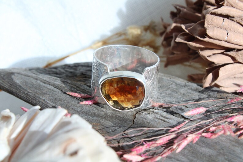 May include: A silver ring with an intricate design and a large, faceted, amber-colored gemstone.
