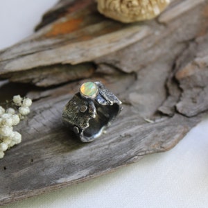 May include: A silver ring with a textured, organic design and a round, iridescent opal gemstone.