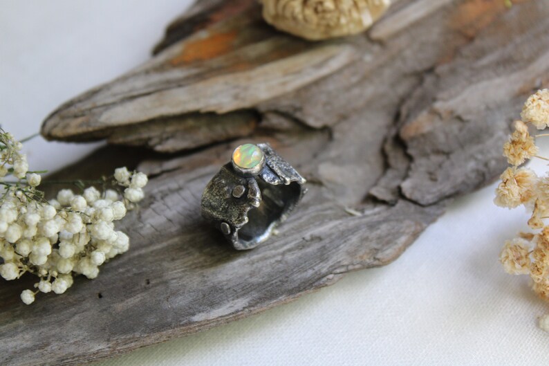 May include: A silver ring with a textured, organic design and a round, iridescent opal gemstone.