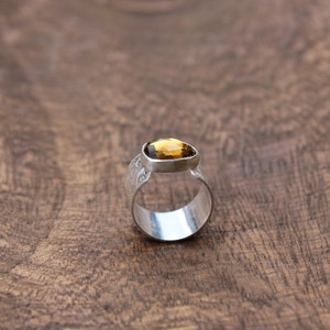 May include: A silver ring with a textured band and a faceted, amber-colored gemstone.