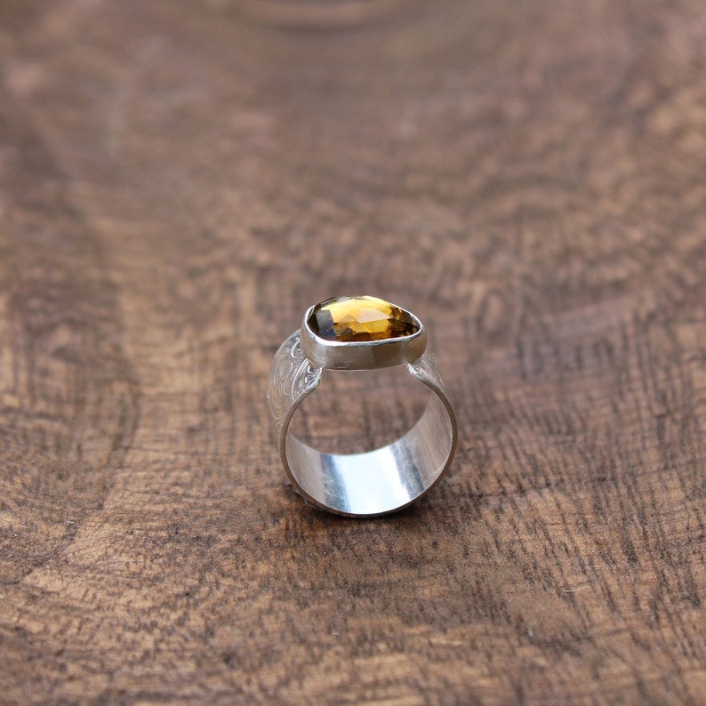 May include: A silver ring with a textured band and a faceted, amber-colored gemstone.