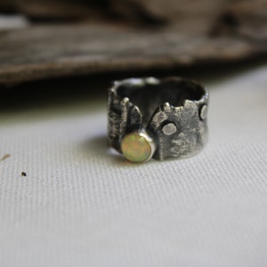 May include: A silver ring with a textured, tree bark-like design and a round, pale yellow opal stone.