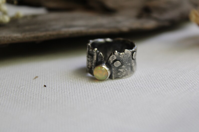 May include: A silver ring with a textured, tree bark-like design and a round, pale yellow opal stone.