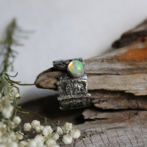May include: A silver ring with a textured band and a round, green opal gemstone.