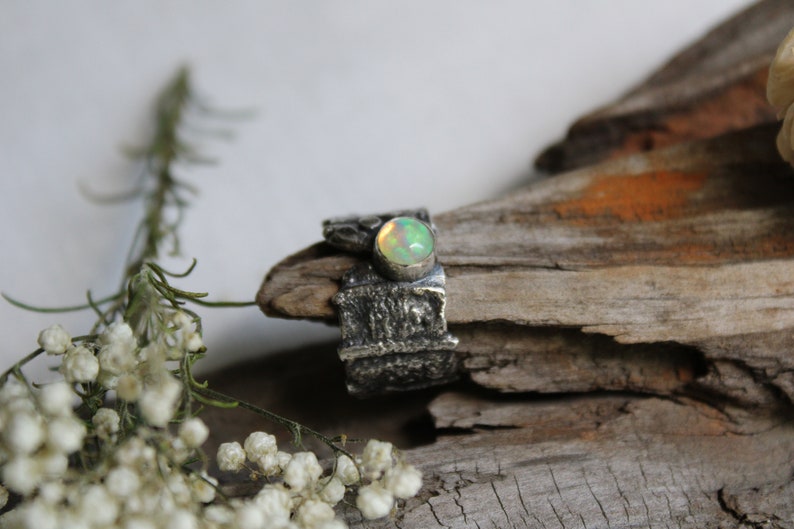 May include: A silver ring with a textured band and a round, green opal gemstone.