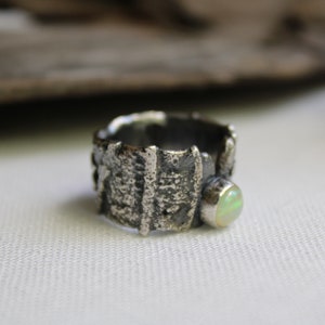 May include: A silver ring with a textured, organic design and a pale green opal stone.