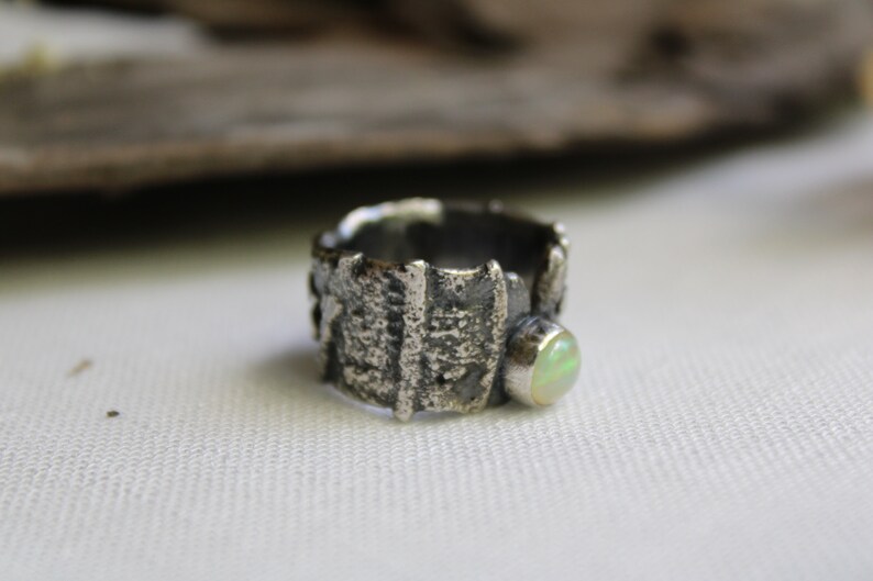 May include: A silver ring with a textured, organic design and a pale green opal stone.