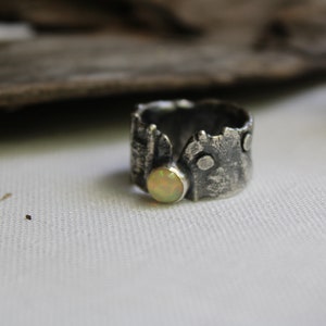 May include: A silver ring with a textured, tree bark-like design and a round, pale yellow opal gemstone.