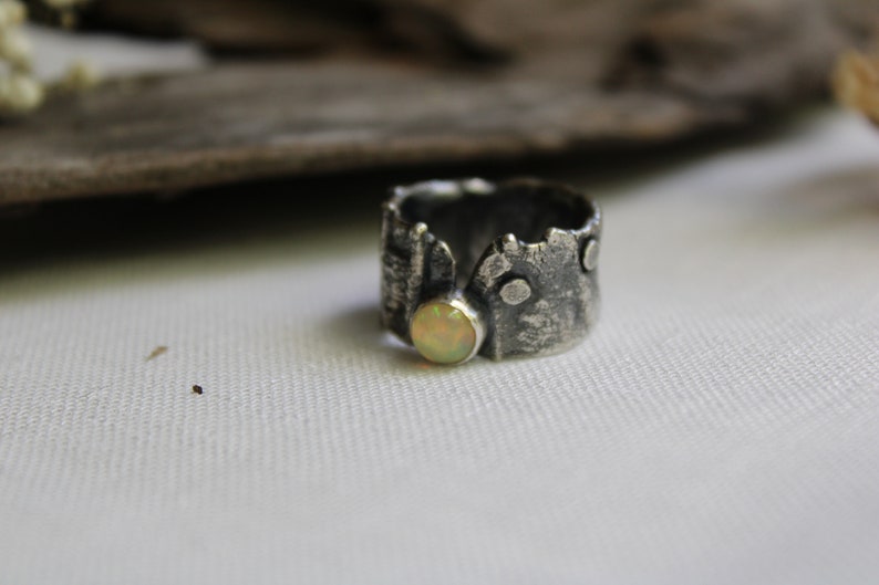 May include: A silver ring with a textured, tree bark-like design and a round, pale yellow opal gemstone.