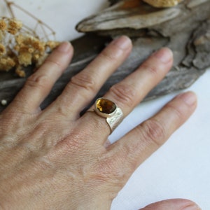 May include: A silver ring with a large, oval-shaped, amber-colored gemstone. The ring has a textured band.
