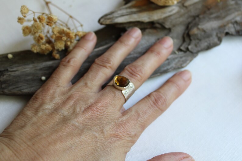 May include: A silver ring with a large, oval-shaped, amber-colored gemstone. The ring has a textured band.