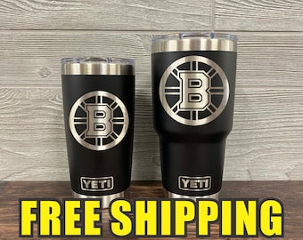 May include: Two black Yeti tumblers with silver accents. Each tumbler features the Boston Bruins logo, a silver "B" inside a circle. The Yeti logo is at the bottom. The text "FREE SHIPPING" is at the bottom.