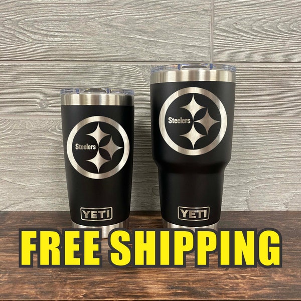 Op de afbeelding: Twee zwarte YETI bekers met roestvrijstalen deksels en een zilveren Steelers-logo. De kleinere beker is 20 oz en de grotere beker is 30 oz. De bekers staan op een houten oppervlak met de tekst "GRATIS VERZENDING" in gele letters.