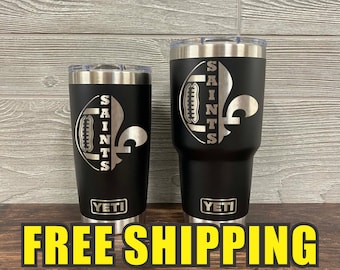 May include: Two stainless steel tumblers with black powder coating and a silver design of a football and the word "Saints" with a fleur-de-lis. The tumblers have the word "YETI" printed on the bottom.