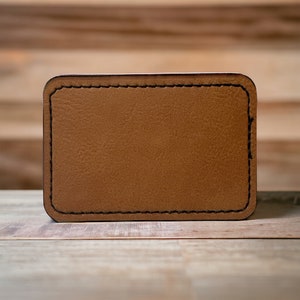 May include: A brown leather patch with a stitched border. The patch is blank and ready for personalization.