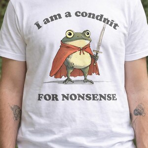 May include: White t-shirt with a cartoon frog wearing a red cape and holding a sword. The text on the shirt reads "I am a conduit FOR NONSENSE."