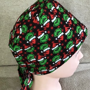 May include: A black, red, and green patterned surgical scrub hat with a repeating pattern of the Grinch wearing a Santa hat.