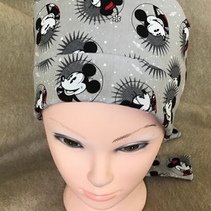 May include: Gray scrub hat with a Mickey Mouse print. The hat has a tie on the back.