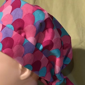 Könnte beinhalten: Eine rosa, lila und blaue gemusterte OP-Mütze mit Schleife. Das Muster besteht aus überlappenden Kreisen.