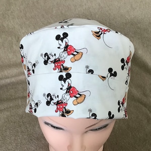 May include: White scrub hat with a repeating pattern of Mickey Mouse and Minnie Mouse in red, black, and white.