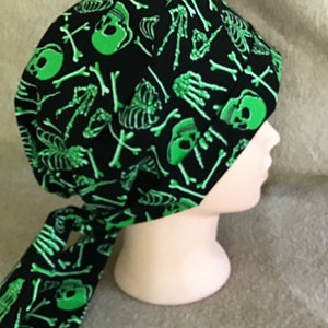 May include: A black scrub hat with a green skull and crossbones pattern. The hat has a tie that is also patterned.