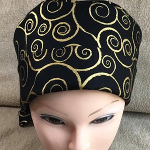 May include: Black scrub hat with a gold swirl pattern.