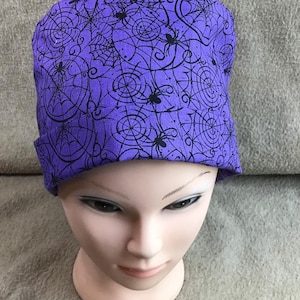 May include: Purple scrub hat with a black spiderweb and spider pattern.