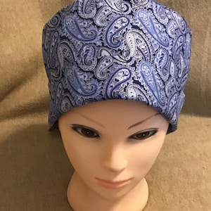 May include: A blue and white paisley patterned scrub cap. The cap is made of fabric and is designed to be worn on the head. The cap is displayed on a mannequin head.