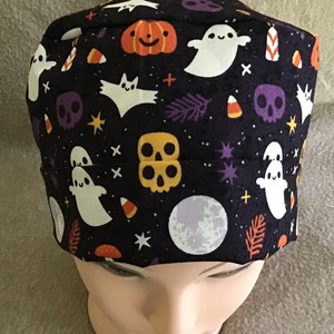 Könnte beinhalten: Eine schwarze OP-Mütze mit einem Halloween-Motiv mit Geistern, Fledermäusen, Totenköpfen, Kürbissen, Maisbonbons und Sternen.
