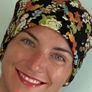 Könnte beinhalten: Ein schwarzer Stoffhut mit einem floralen Muster in Braun-, Orange-, Grün- und Weißtönen. Der Hut wird von einer Person mit hellbraunen Haaren und blauen Augen getragen.