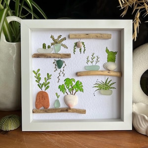 May include: A framed artwork featuring a collection of illustrated potted plants on wooden shelves. The plants are depicted in various styles, with green foliage and colorful pots. The frame is white, and the background is white.