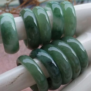 May include: A stack of jade rings in various shades of green. The rings are smooth and polished, with a glossy finish.
