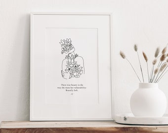 May include: A white framed print with a black line drawing of a person with flowers growing from their head. The quote "There was beauty in the way she wore her vulnerability" by Brené Brown is printed below the drawing.