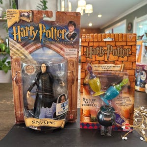 May include: A Harry Potter and the Sorcerer's Stone Professor Snape action figure in original packaging next to a Harry Potter Snape's Potions Candy set. The Snape figure wears a black robe, and the candy set includes a black cauldron and two bottles.