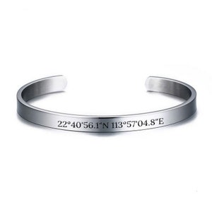May include: A silver bangle bracelet with the coordinates "22°40'56.1"N 113°57'04.8"E" engraved on it.