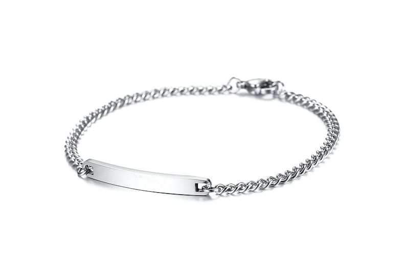 May include: A silver-toned metal chain bracelet featuring a smooth, rectangular identification bar at the center. The bracelet is constructed with small, interlocking links and includes a secure lobster claw clasp closure at the back.