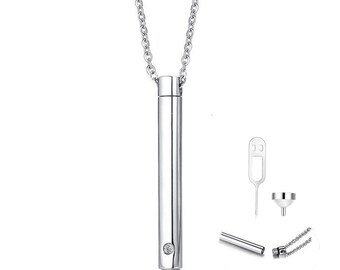 May include: A silver chain necklace with a small, cylindrical pendant that has a single, clear stone set into it. The pendant is hollow and can be opened to hold a small amount of ashes or other mementos.