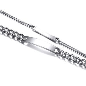 May include: Two silver-toned metal bracelets featuring a polished, curved identification plate at the center. Each bracelet is constructed with a classic curb chain link design, showcasing a reflective, smooth surface and a metallic finish.