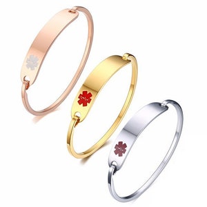 May include: Three medical alert bracelets in different colours: rose gold, gold, and silver. Each bracelet has a rectangular plate with a red medical symbol.