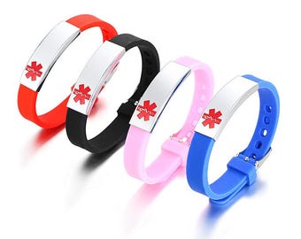 Op de afbeelding: Vier medische waarschuwingsarmbanden in rood, zwart, roze en blauw. Elke armband heeft een zilveren metalen plaat met een rood medisch symbool. De bandjes zijn gemaakt van flexibel materiaal en hebben een gespsluiting.