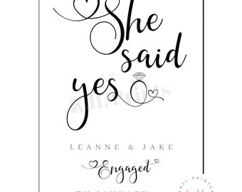 May include: Black and white printable sign with the text "She said yes" in cursive script. The sign also includes a diamond ring and hearts. The text "Leanne & Jake Engaged" and the date "15th January 2021" are also included.