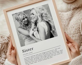 May include: Black and white photo of two sisters smiling at each other. The photo is framed with a white mat and a light wood frame. The text below the photo reads "Sister [Vicky] noun A female sibling and your biggest protector. The one who you share a closeness with that no one else understands. Someone who understands you better than anyone and can make you laugh until you cry. The one who will love you, protect you and drive you crazy all at the same time. A best friend for life."
