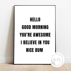 Peut inclure: Une affiche encadrée avec un fond blanc et du texte noir. Le texte se lit comme suit : "HELLO GOOD MORNING YOU'RE AWESOME I BELIEVE IN YOU NICE BUM." Un petit logo circulaire se trouve dans le coin inférieur droit.