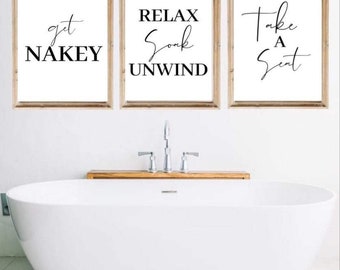 May include: Three framed prints with white backgrounds and black text. The prints are hung on a white wall above a white bathtub. The text on the prints reads "get naky", "relax soak unwind", and "take a seat".