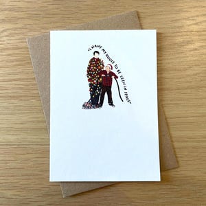 May include: A white card with a brown envelope. The card features a cartoon illustration of two people standing next to a Christmas tree with lights. The text on the card reads "I want my house to be seen in space."