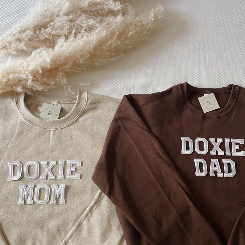 May include: Two sweatshirts with the words "Doxie Mom" and "Doxie Dad" in white letters on a beige and brown sweatshirt, respectively.
