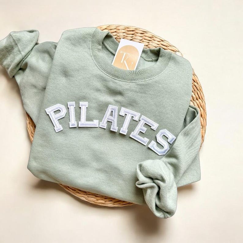 May include: A light green sweatshirt with the word "PILATES" in white letters on the front.