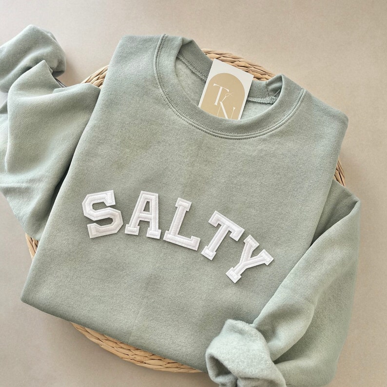 May include: A sage green sweatshirt with the word "SALTY" in white felt letters.