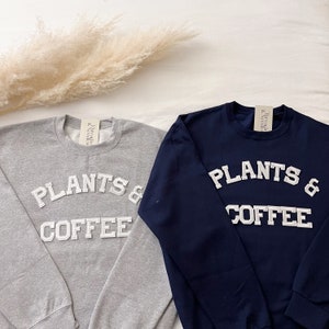 May include: A white ceramic mug with a black handle and the text "But First, Coffee" in a bold, black font. The mug is filled with a dark liquid, likely coffee, and sits on a light-colored surface.