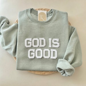 May include: Sage green sweatshirt with the words "God is Good" in white outlined letters.